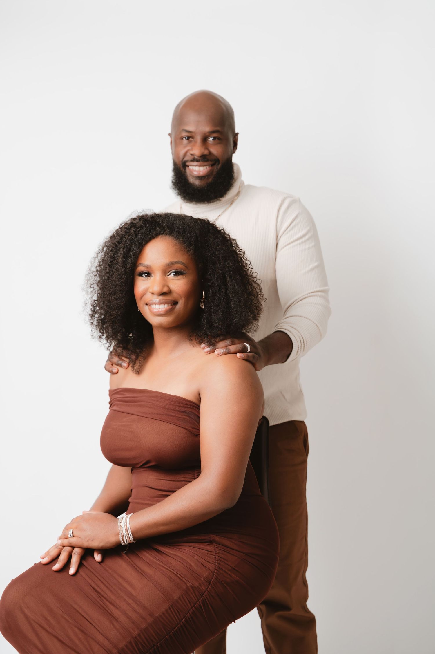 A couple poses together in coordinating brown and cream outfits during a romantic studio photoshoot.