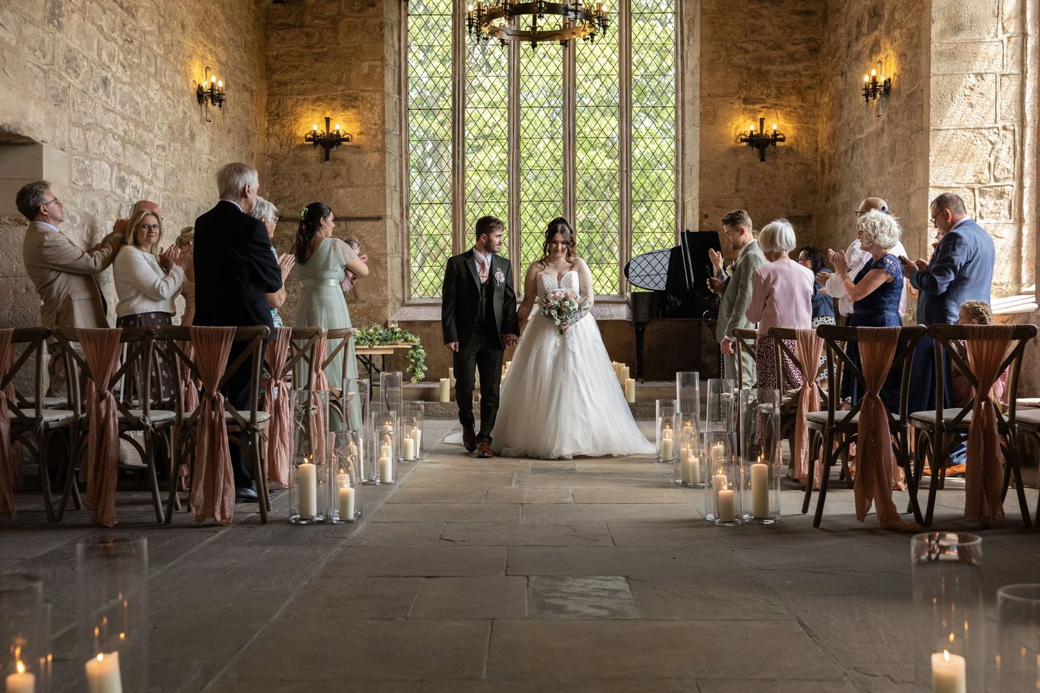 A panoramic view of a rustic stone chapel interior with wall sconces and guests gathered for a wedding ceremony.