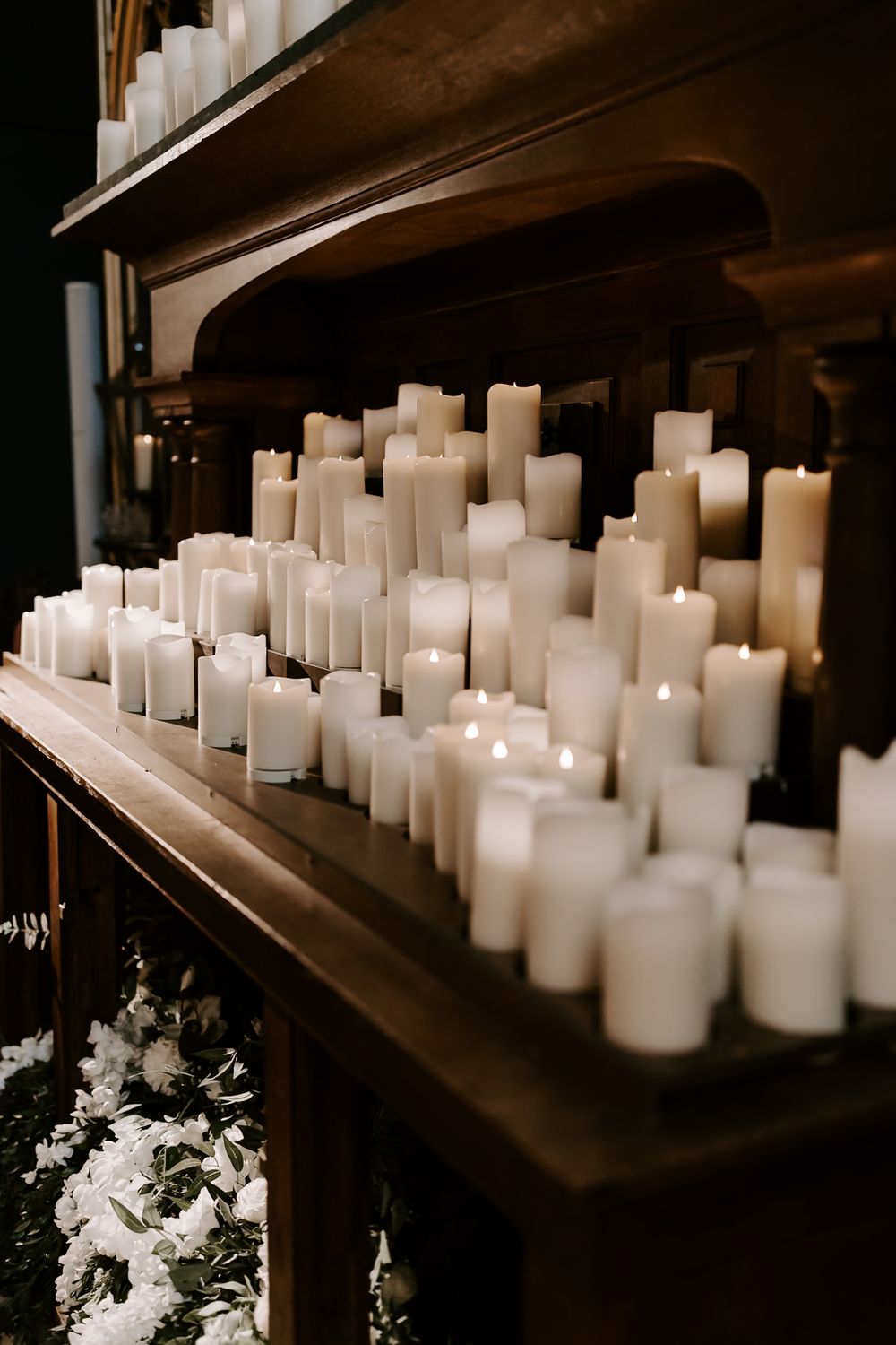 White pillar candles arranged in rows on dark wooden shelves create an elegant and moody ambiance.