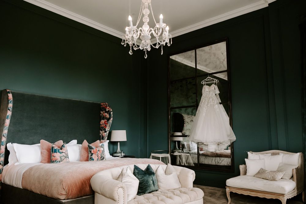 Elegant bedroom interior with dark emerald green walls, white bedding, and crystal chandelier creating moody ambiance.