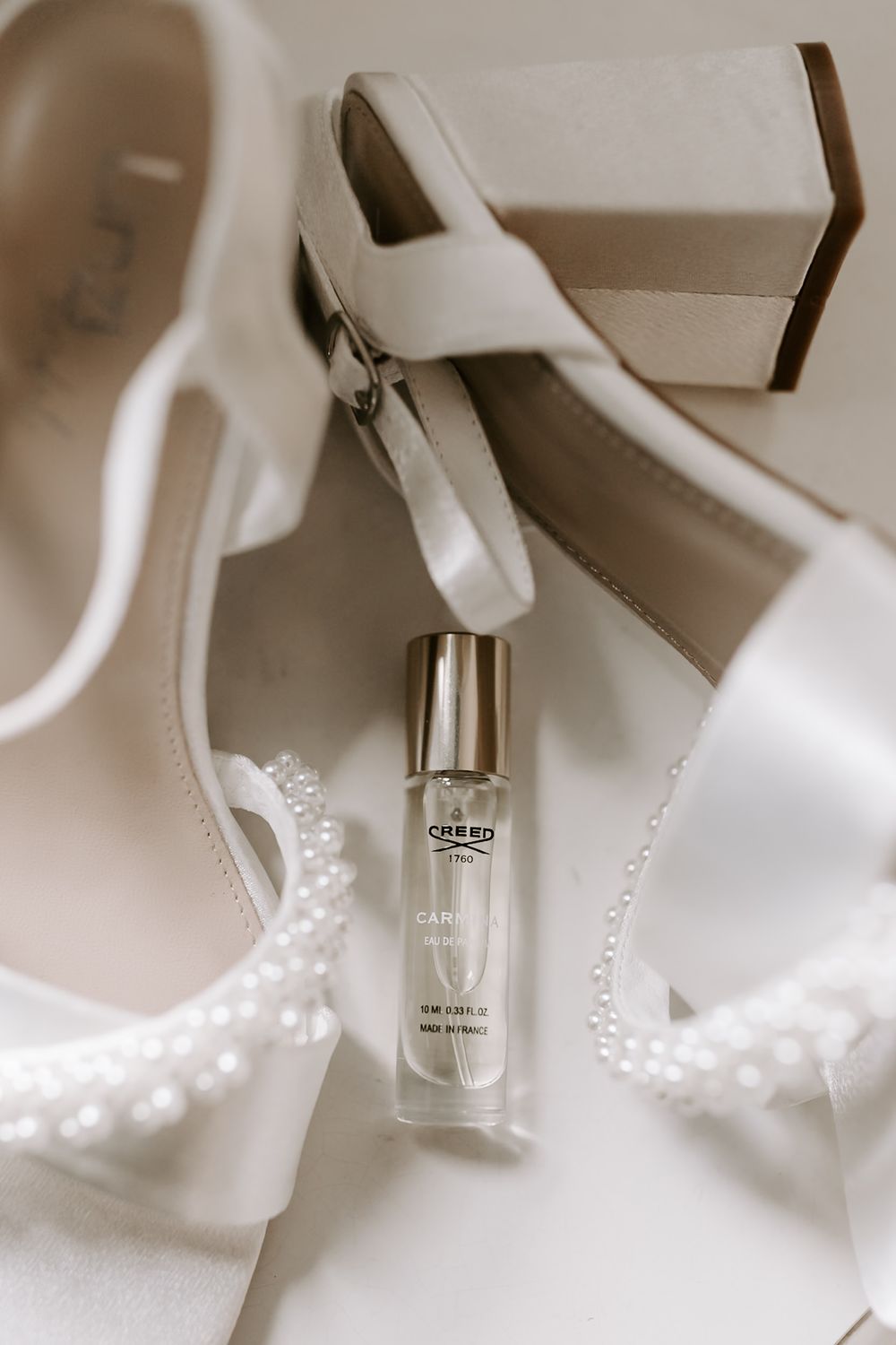 A perfume bottle nestled among delicate white pearls and fabric creates an elegant beauty product composition.