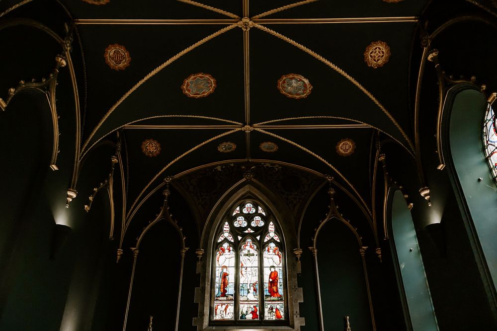 Ornate Gothic cathedral interior with vaulted ceiling, arches, and stained glass windows illuminated in dark lighting.