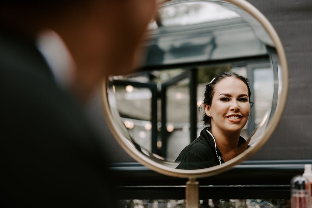 Multiple reflections in oval mirrors show a woman with red lipstick and elegant makeup against a dark background.