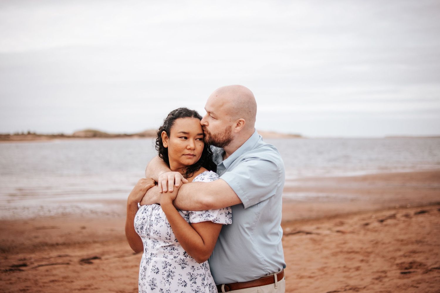 Couple embracing on a sandy beach during sunset with ocean waves in the background.