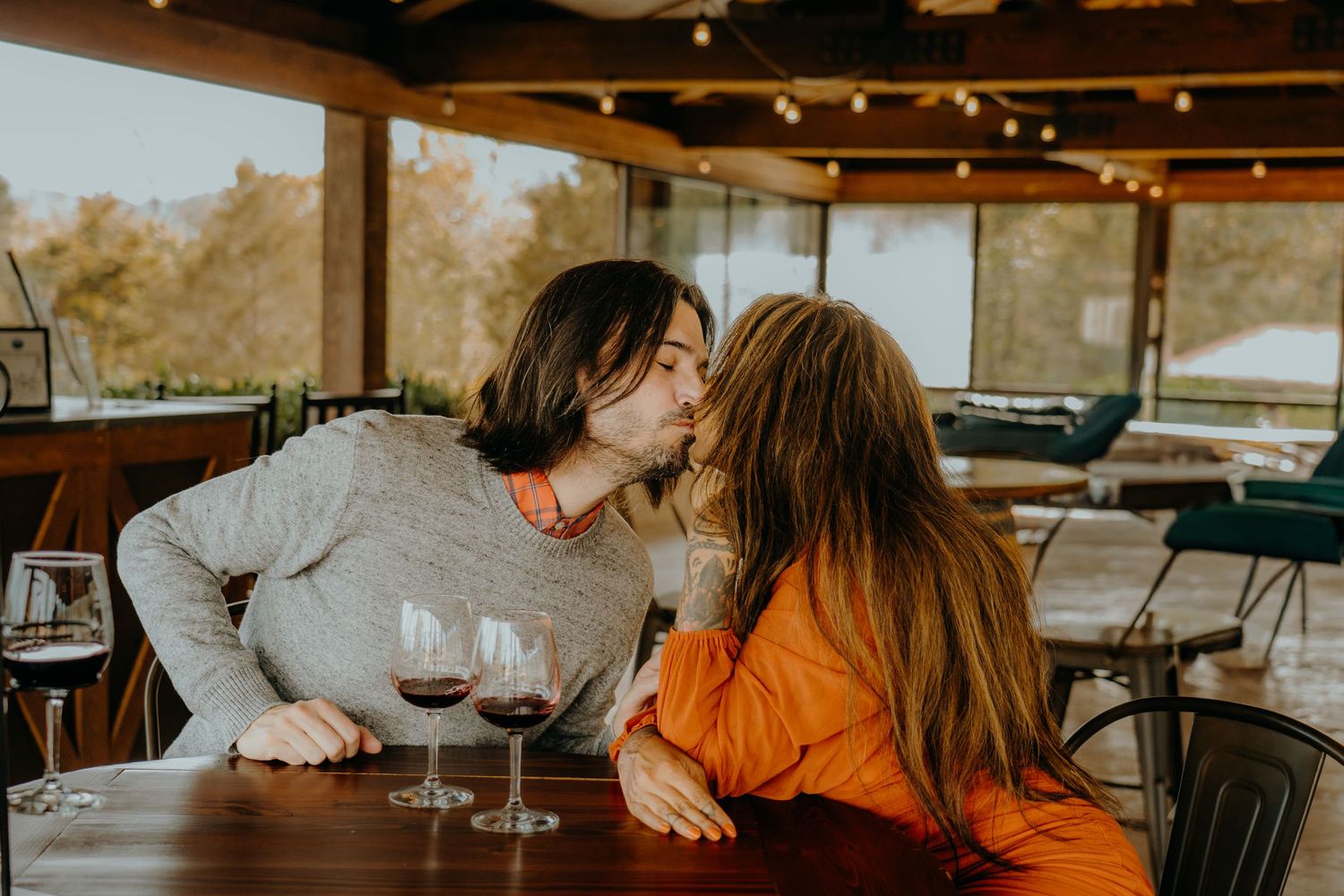 Romantic wine tasting date with couple sitting at wooden table in warm-lit venue.