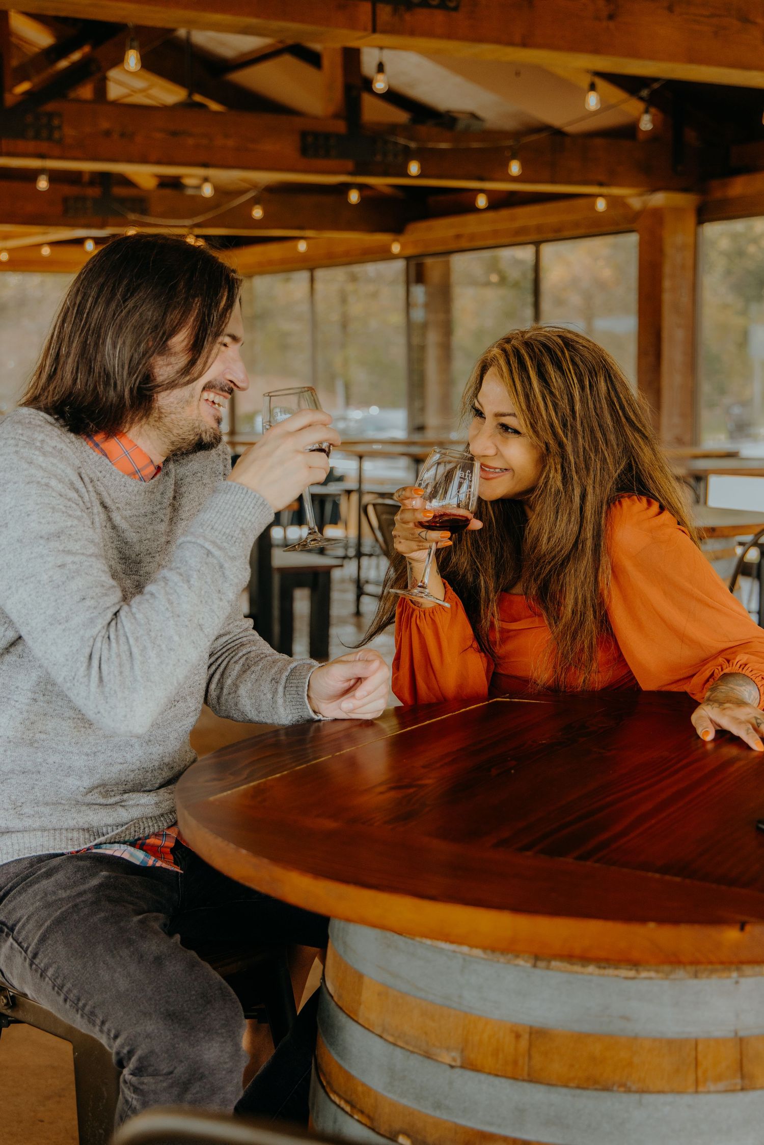 Couple shares intimate moments during wine tasting at rustic wooden table with overhead lighting.