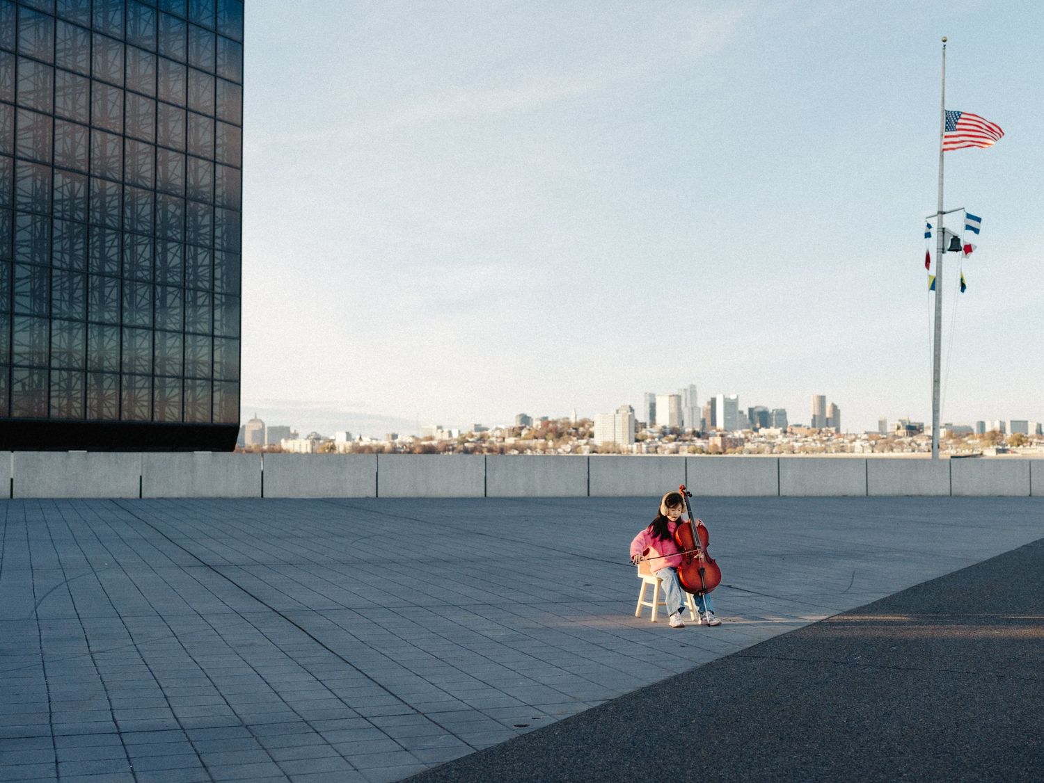 Modern glass building facade reflects sky and cityscape with American flag visible in urban setting.