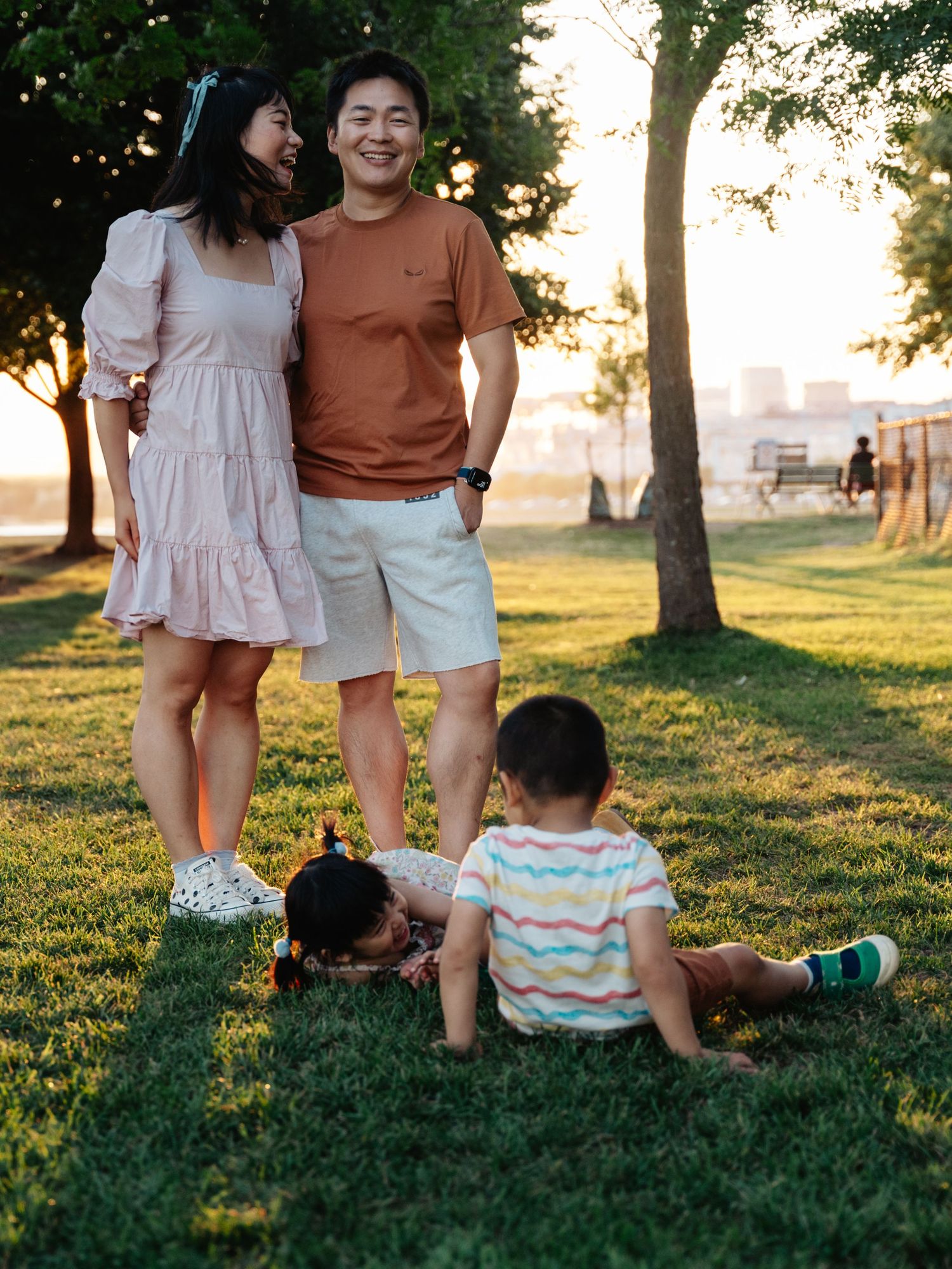 Family enjoys playful moment together on grassy hill during golden sunset in park.