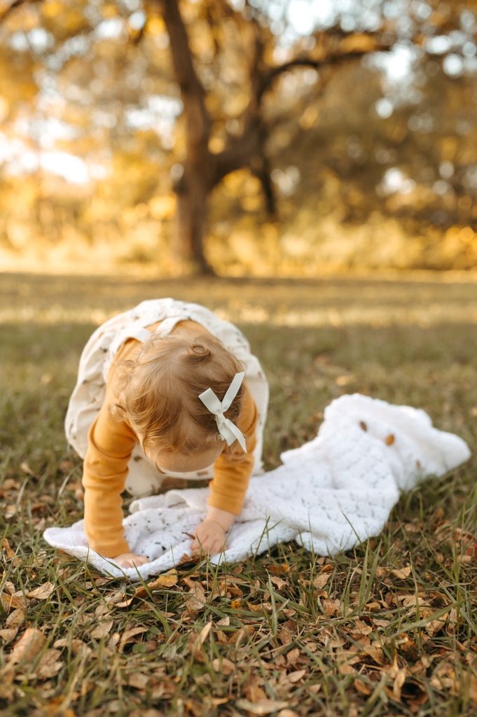 A small child bends down to touch a white blanket on fallen leaves during golden hour.