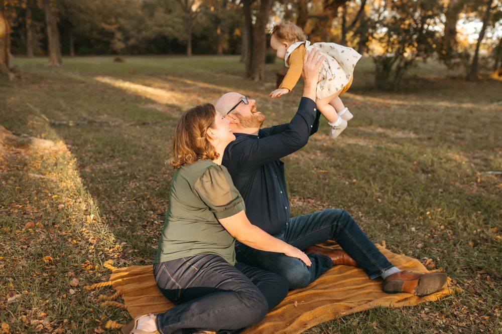 A family relaxes together on a wooden bench in a sunlit autumn park during golden hour.