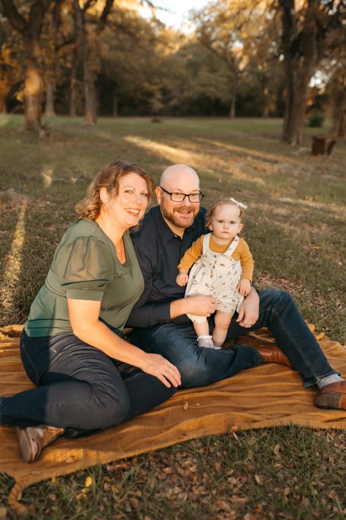 A family shares joyful moments while lounging on a rustic wooden bench surrounded by fallen leaves.