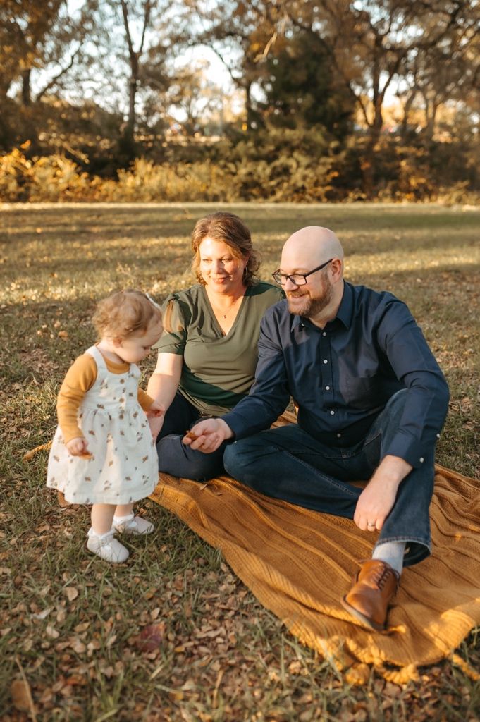 A family relaxes together on a golden blanket in a park during autumn sunset.