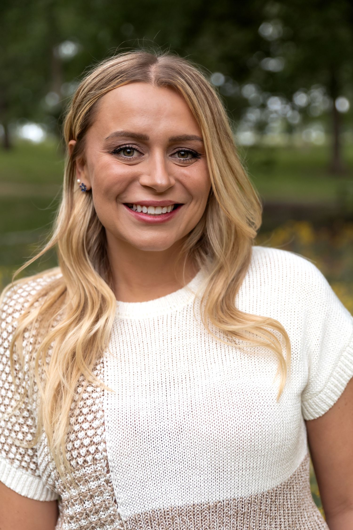 Portrait of someone in a white knit sweater outdoors with a warm smile.