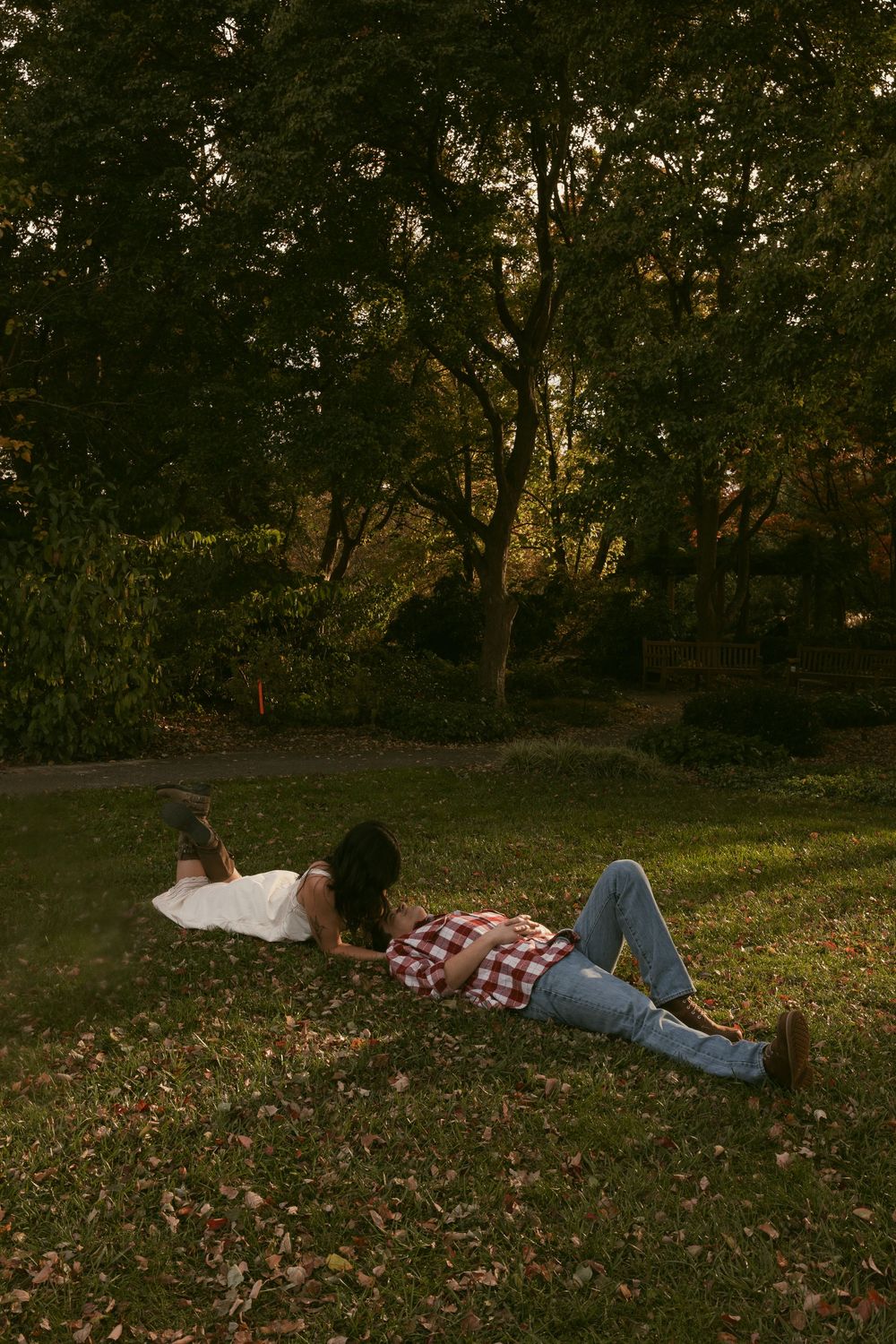 A couple lying together on autumn leaves in a park during golden hour.