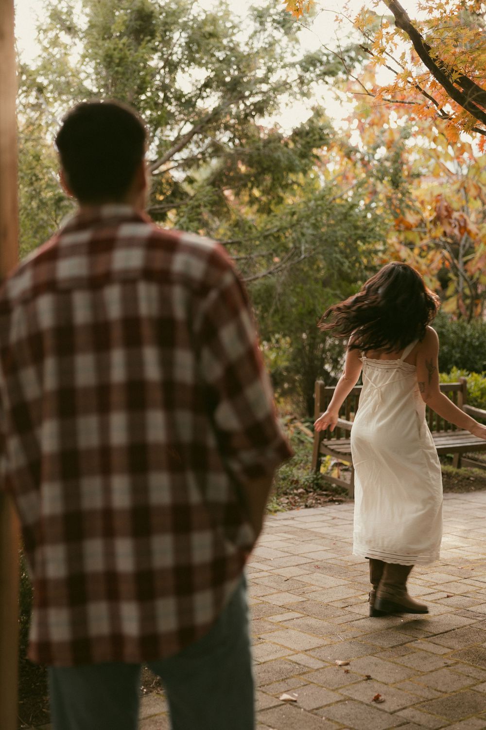 Two people walking together on a stone patio surrounded by autumn trees.