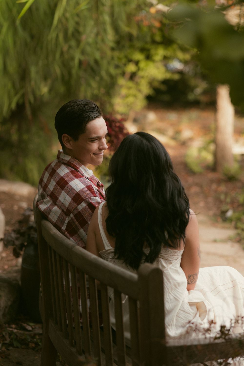Couple sharing a romantic moment on a wooden bench in a garden setting.