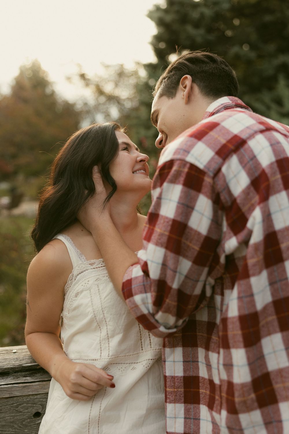 Romantic couple in white dress and plaid shirt sharing an intimate moment outdoors.