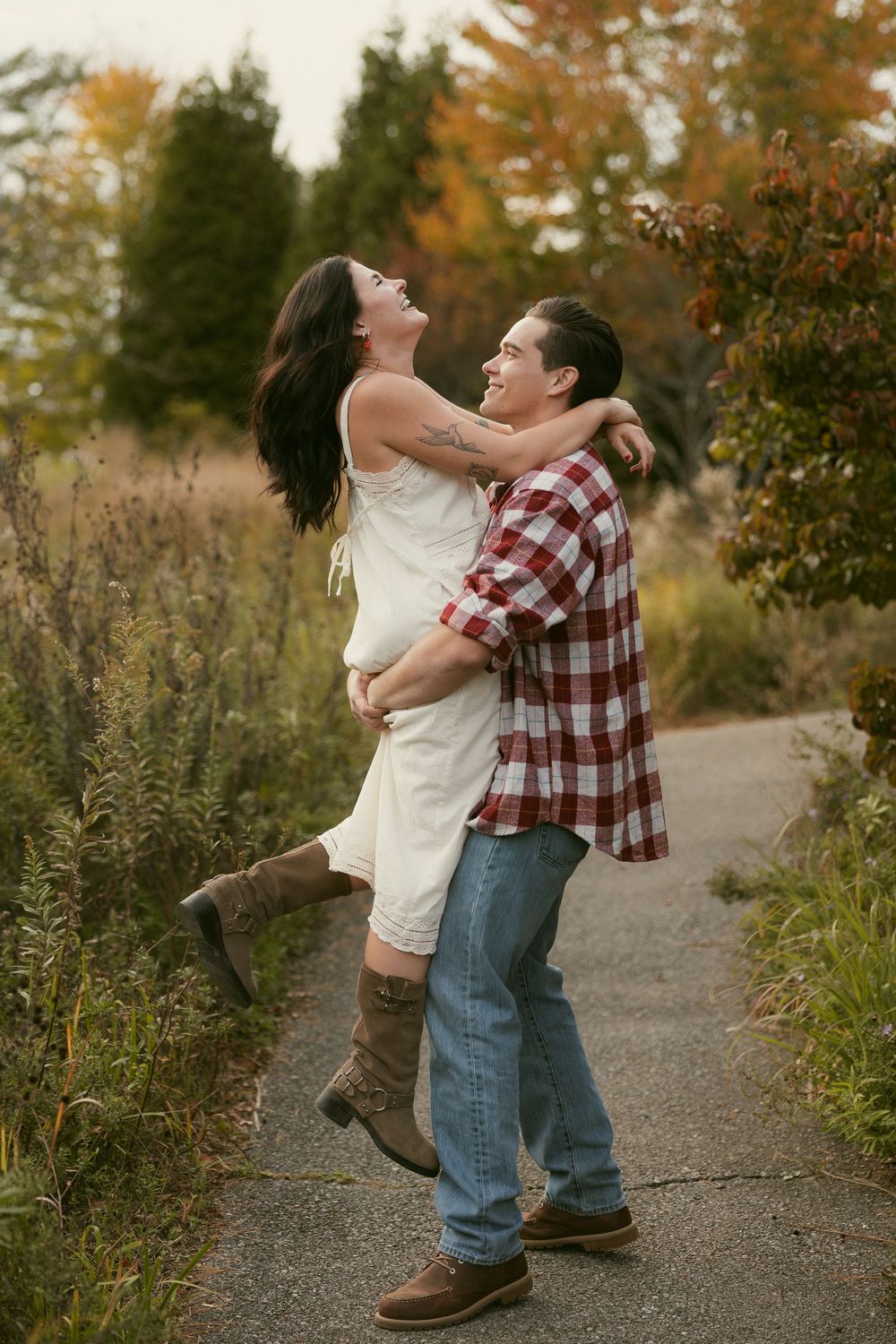 Couple embracing and spinning on a path surrounded by fall foliage.