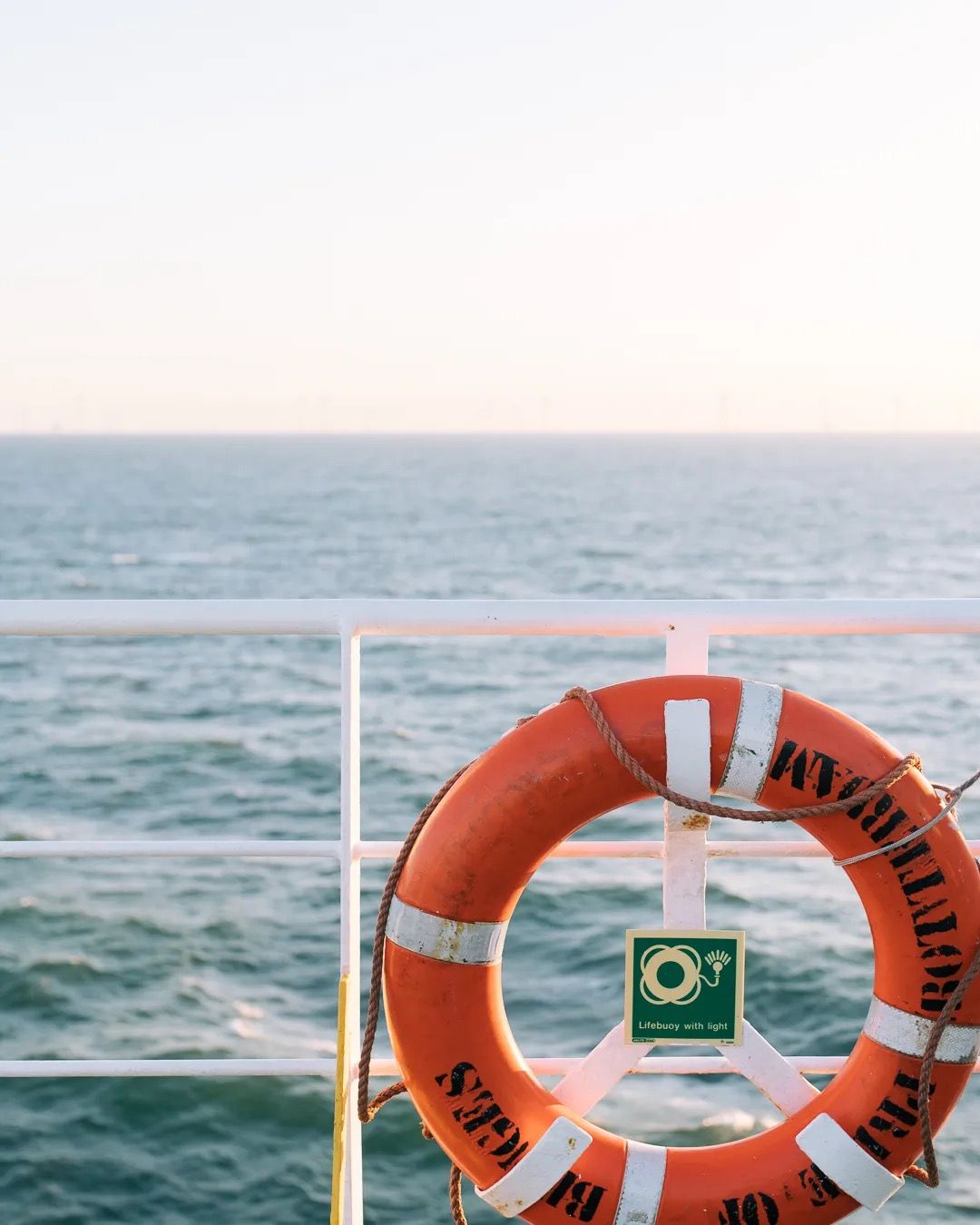 Orange lifebuoy hanging on a ferry railing with soft sunset light over the sea.
