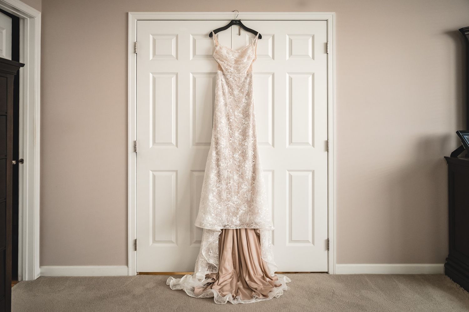 Wedding dress and bridal accessories hanging on white doors in preparation room.