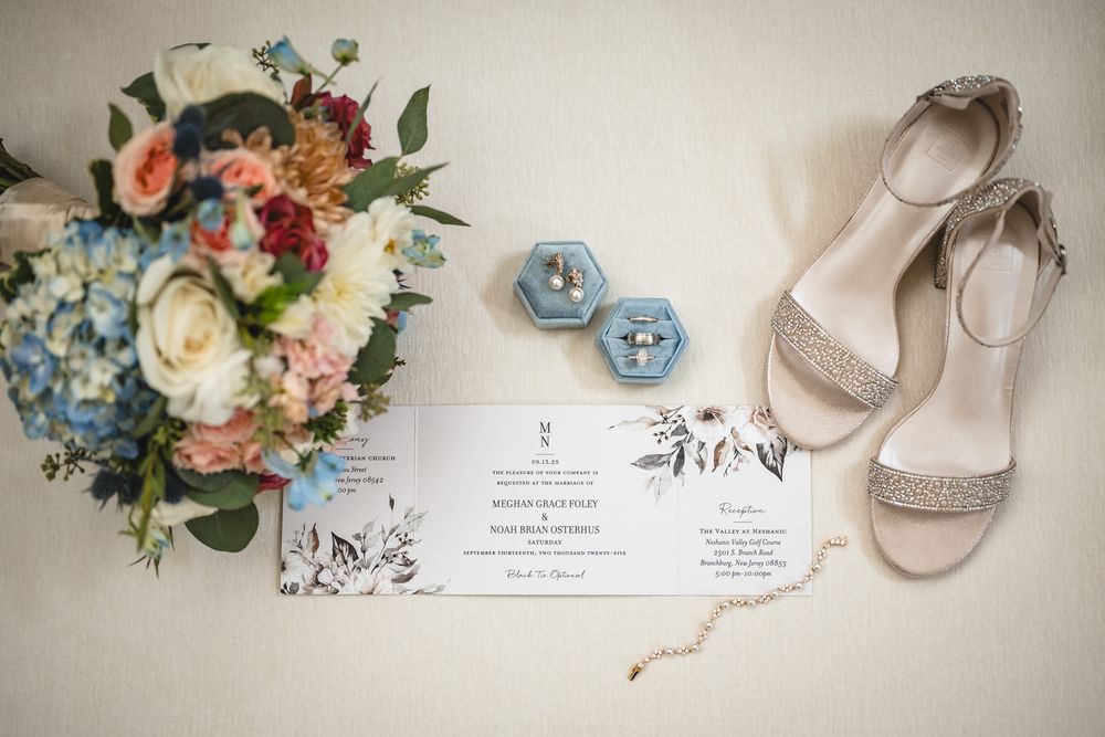 Elegant wedding details including floral arrangements, invitations, and bridal shoes arranged on light background.