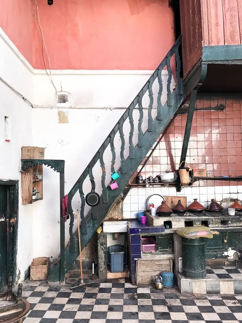A Moroccan courtyard kitchen with tiled floors, open shelving, and a metal staircase.