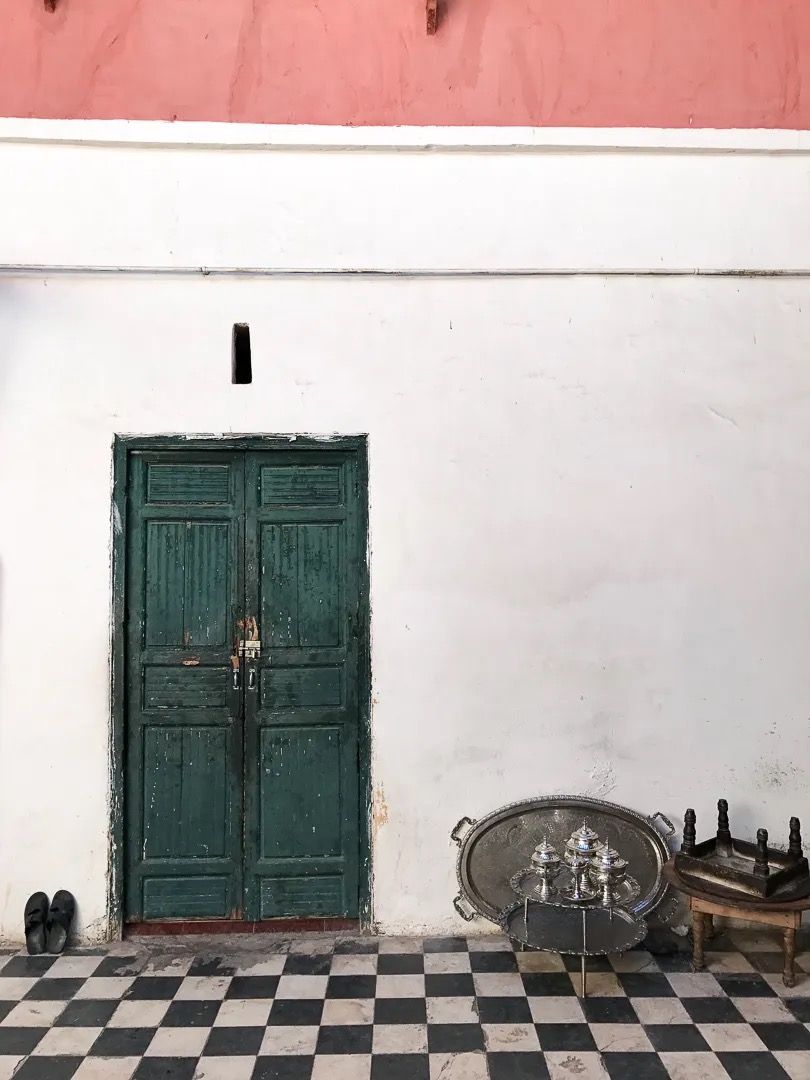 A green metal door set against a white wall with black-and-white checkered tiles.