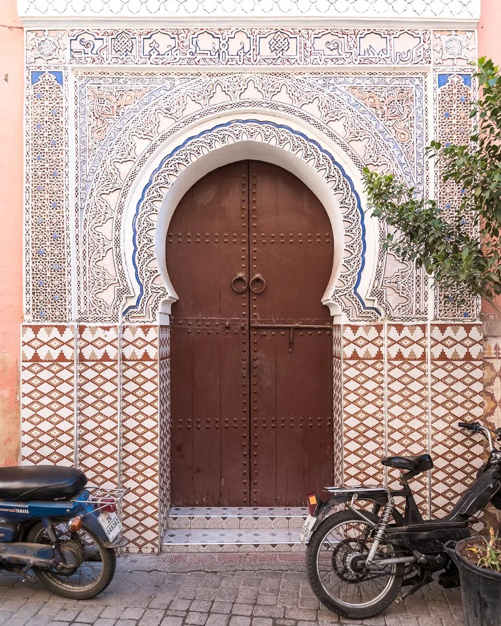A decorative Moroccan arched doorway with patterned tiles and a motorbike parked outside.