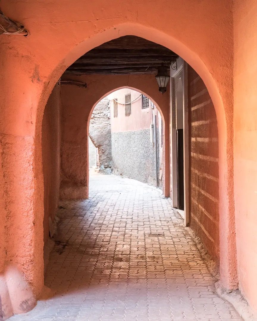 A terracotta arched passageway leading to a narrow alley in a traditional Moroccan street.
