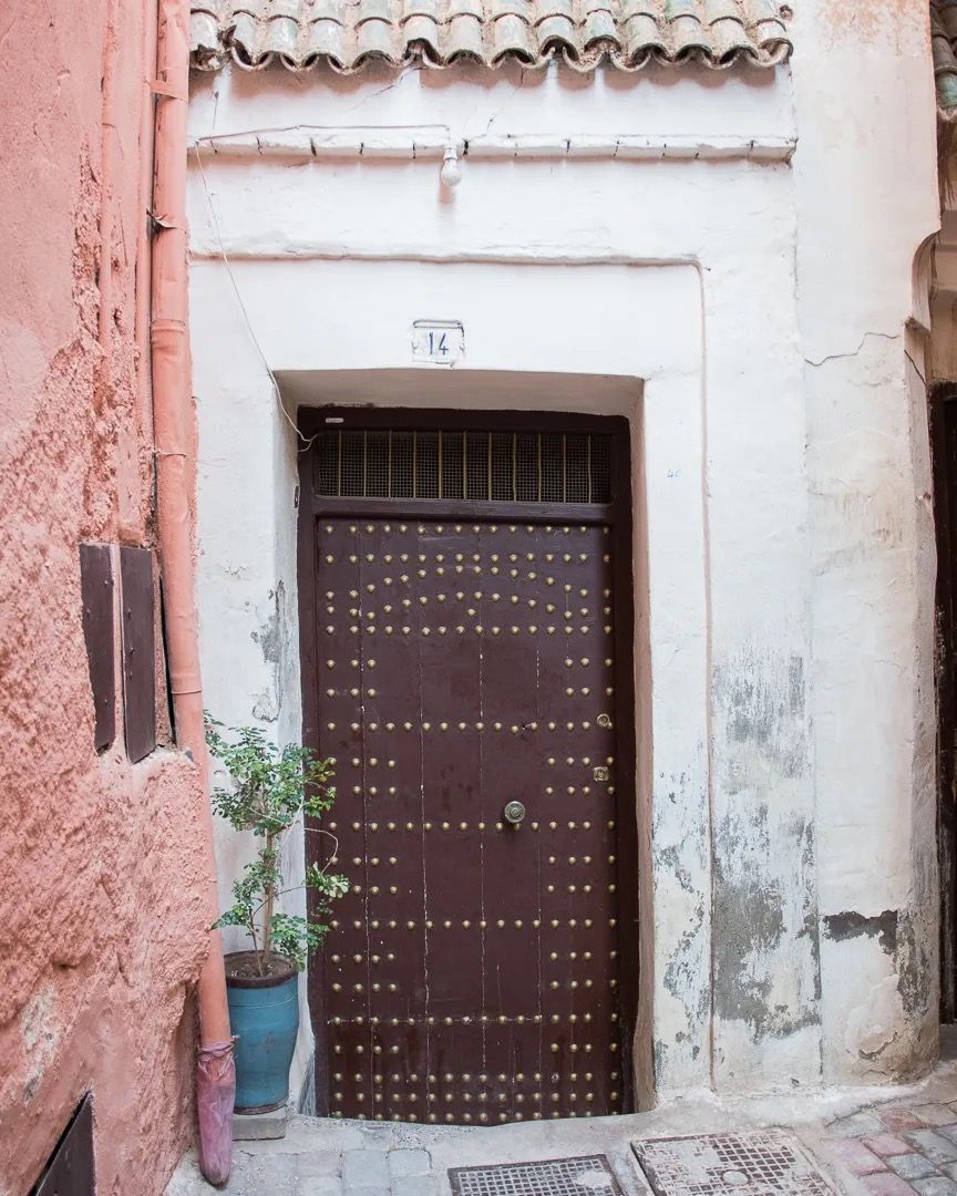 An aged Moroccan doorway featuring a dark wooden door framed by textured pink plaster.