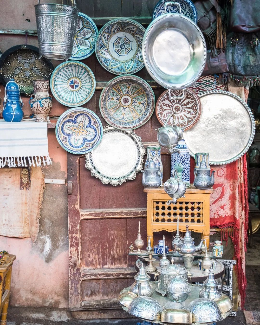 A market stall displaying silver Moroccan teapots, bowls, and handcrafted metalware.