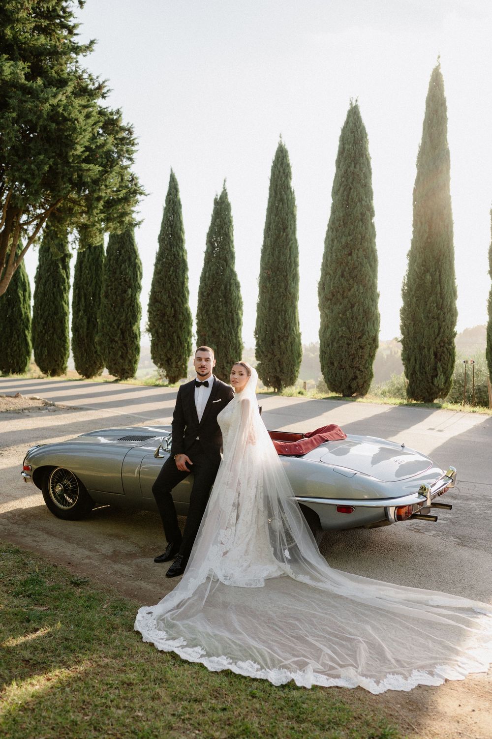 Elegant wedding photo series with vintage car and cypress trees lining a scenic Italian countryside road.