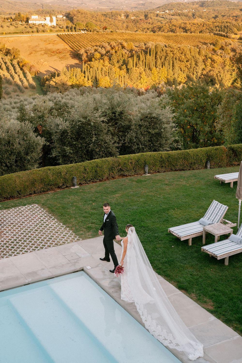 A scenic wedding photoshoot by a pool overlooking a mountainous landscape at golden hour.