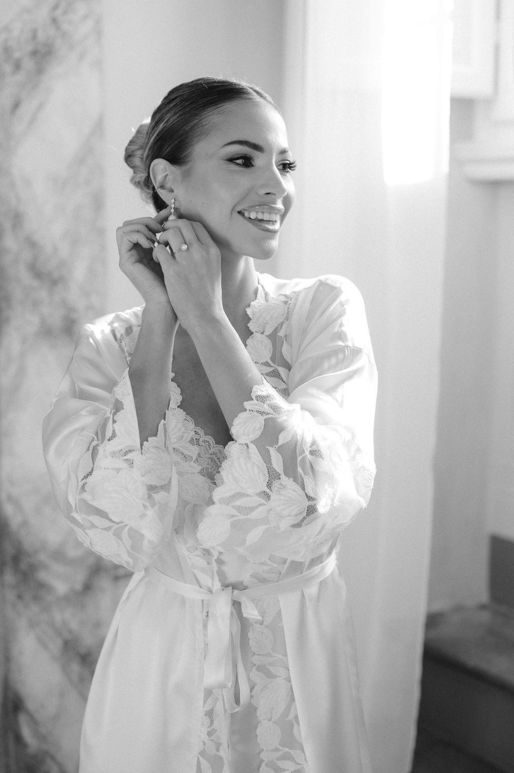 Black and white photo of a bride in a white robe with puffy sleeves getting ready on her wedding day.