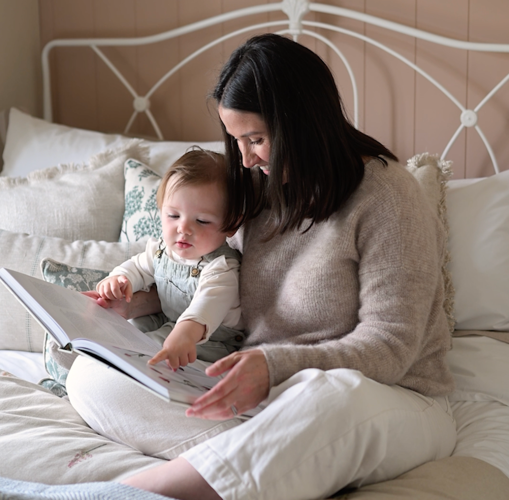 Parent and child reading a book together in bed with white bedding and headboard.