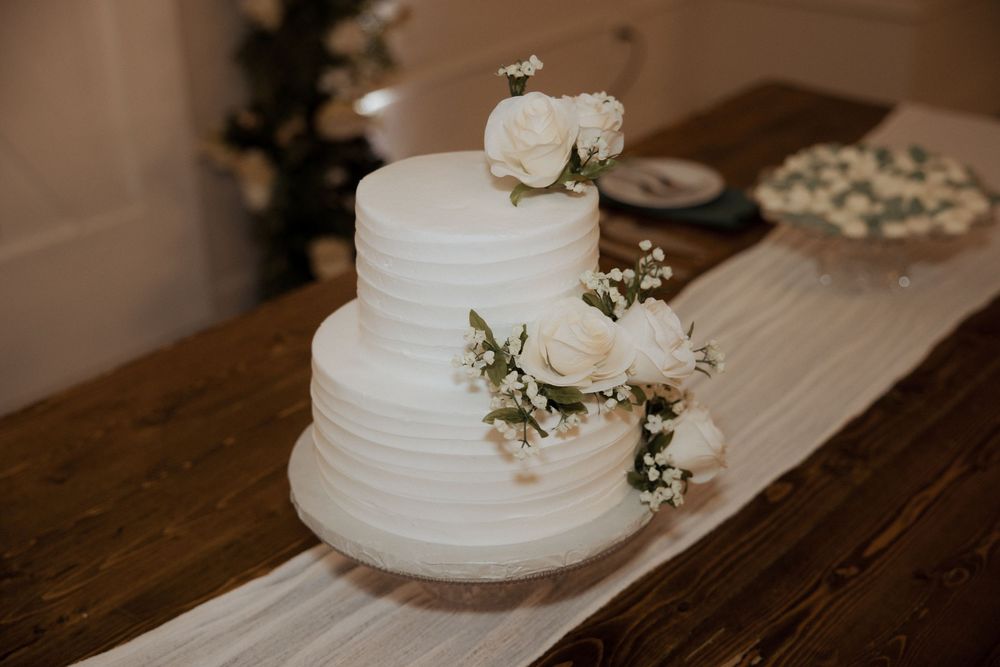 White wedding cake with textured frosting and delicate floral decorations sits on rustic wooden table.