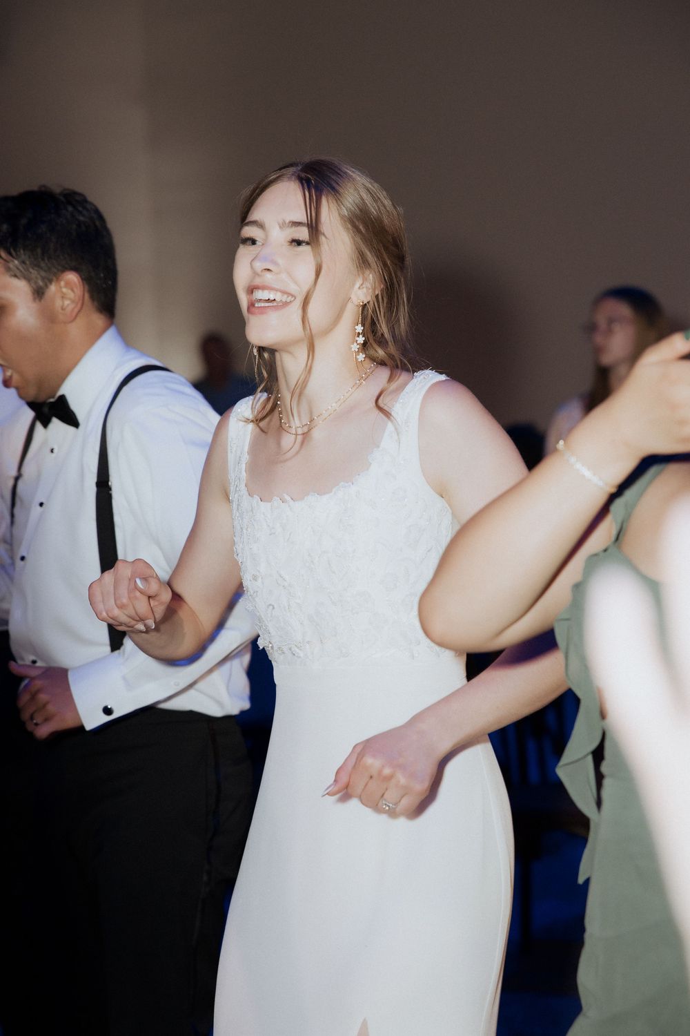 A person in a white wedding dress dances joyfully at a reception while others in formal attire enjoy the celebration.