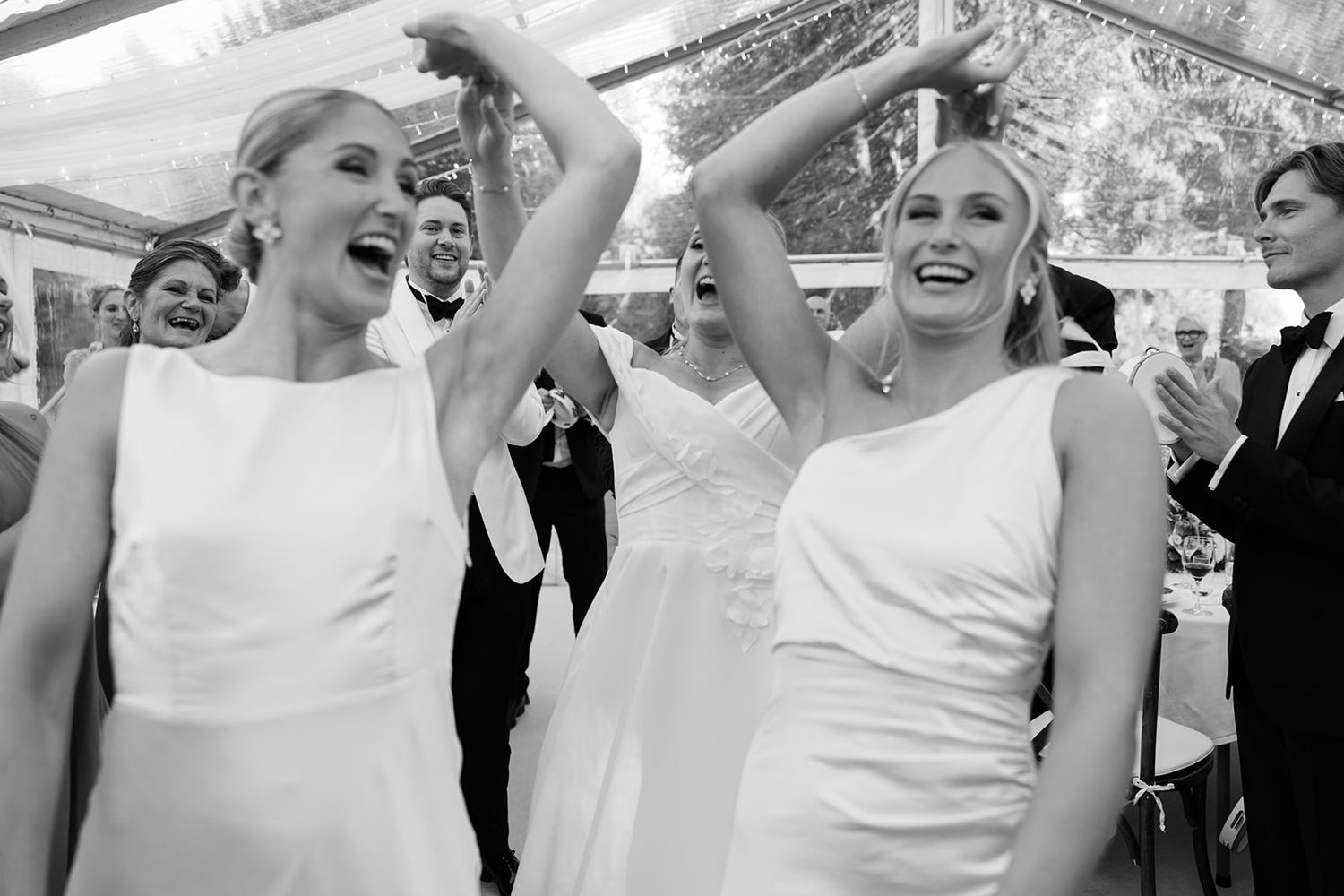 Wedding party dressed in white dances and celebrates joyfully on a dance floor during reception.