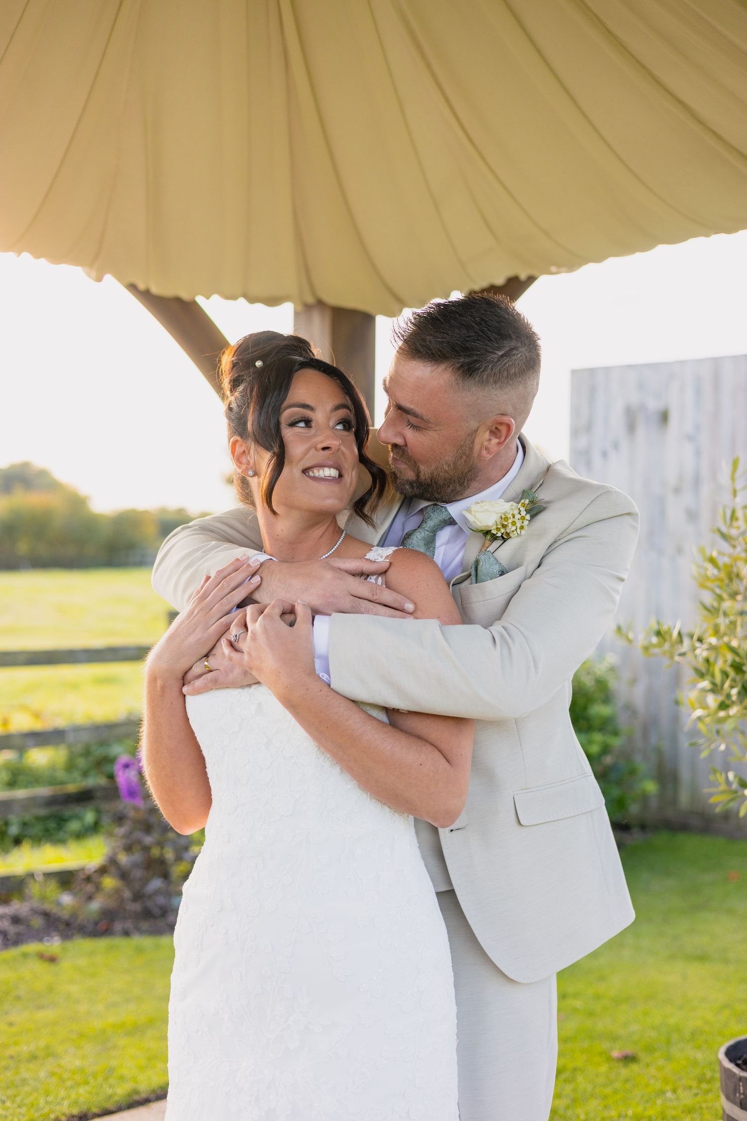 Newlywed couple walking together on a green lawn during golden hour sunset at their outdoor wedding celebration.