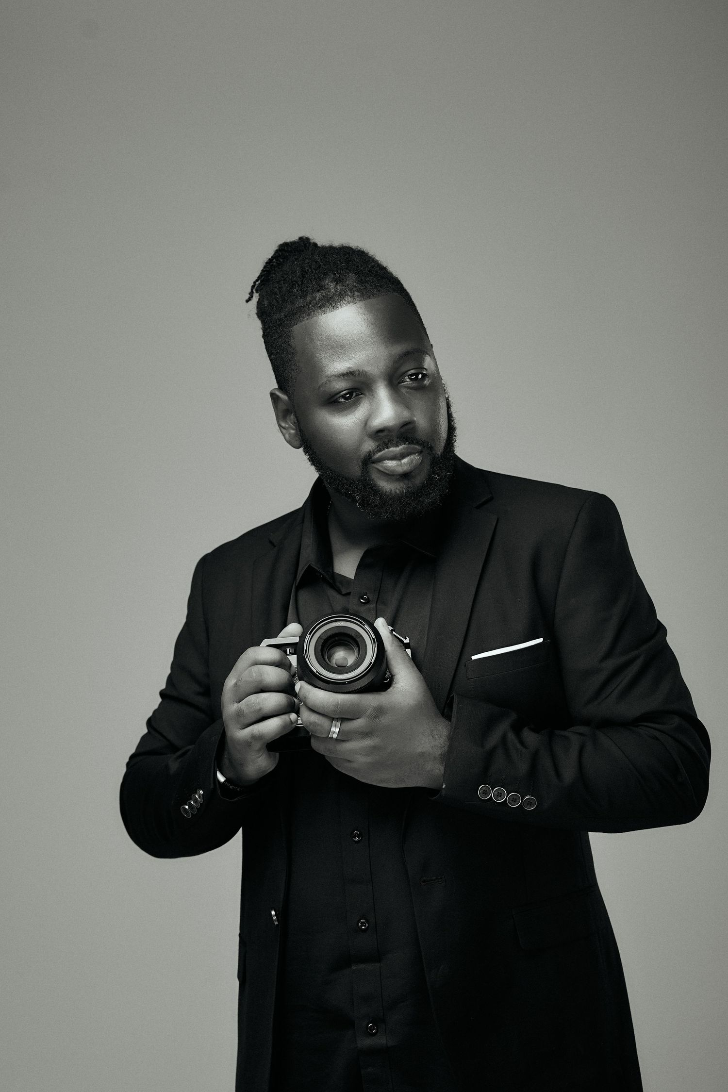 Stylish black and white portrait of a man in a dark suit and watch posing against a neutral background.