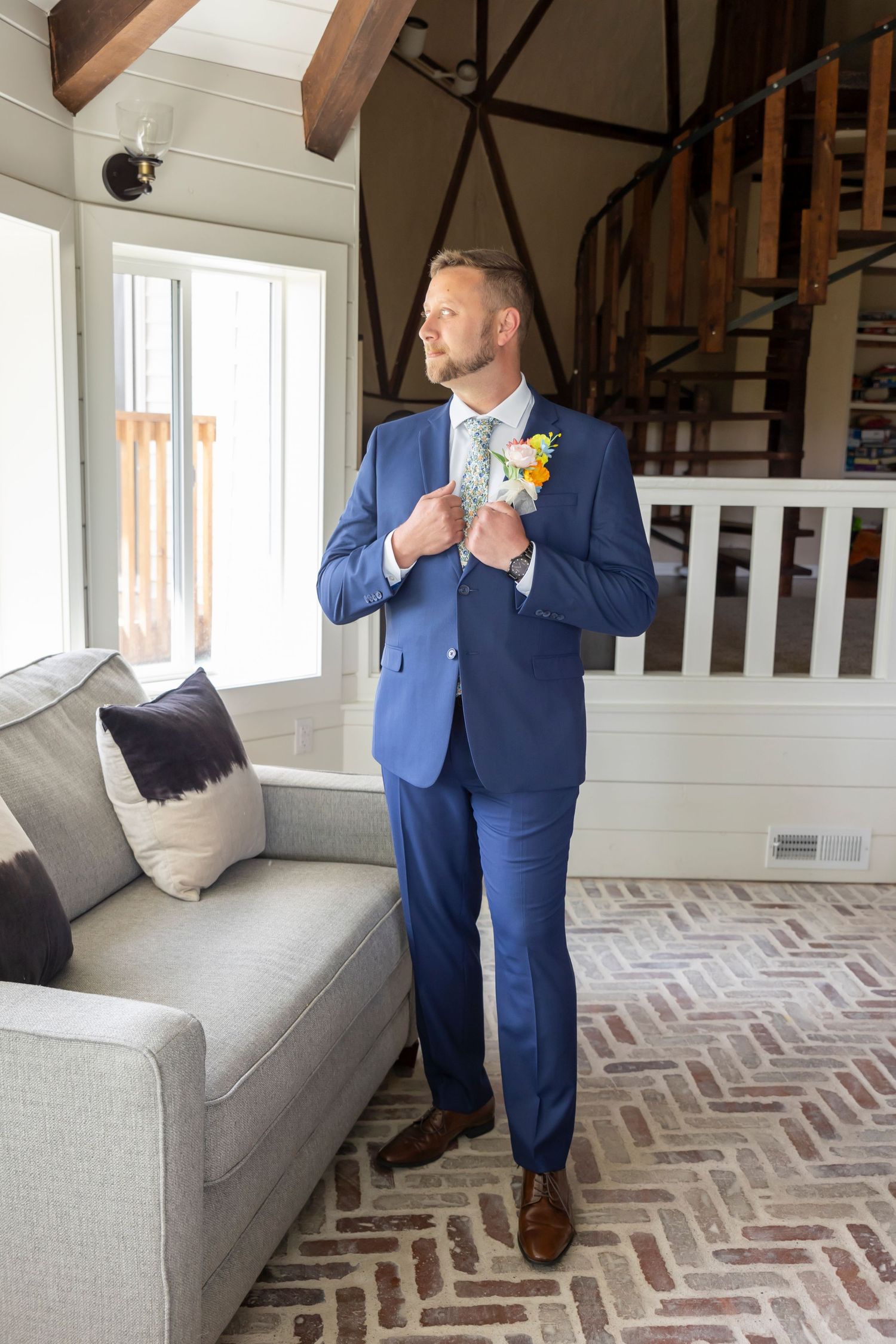 groom in blue suit holding lapel looking out window