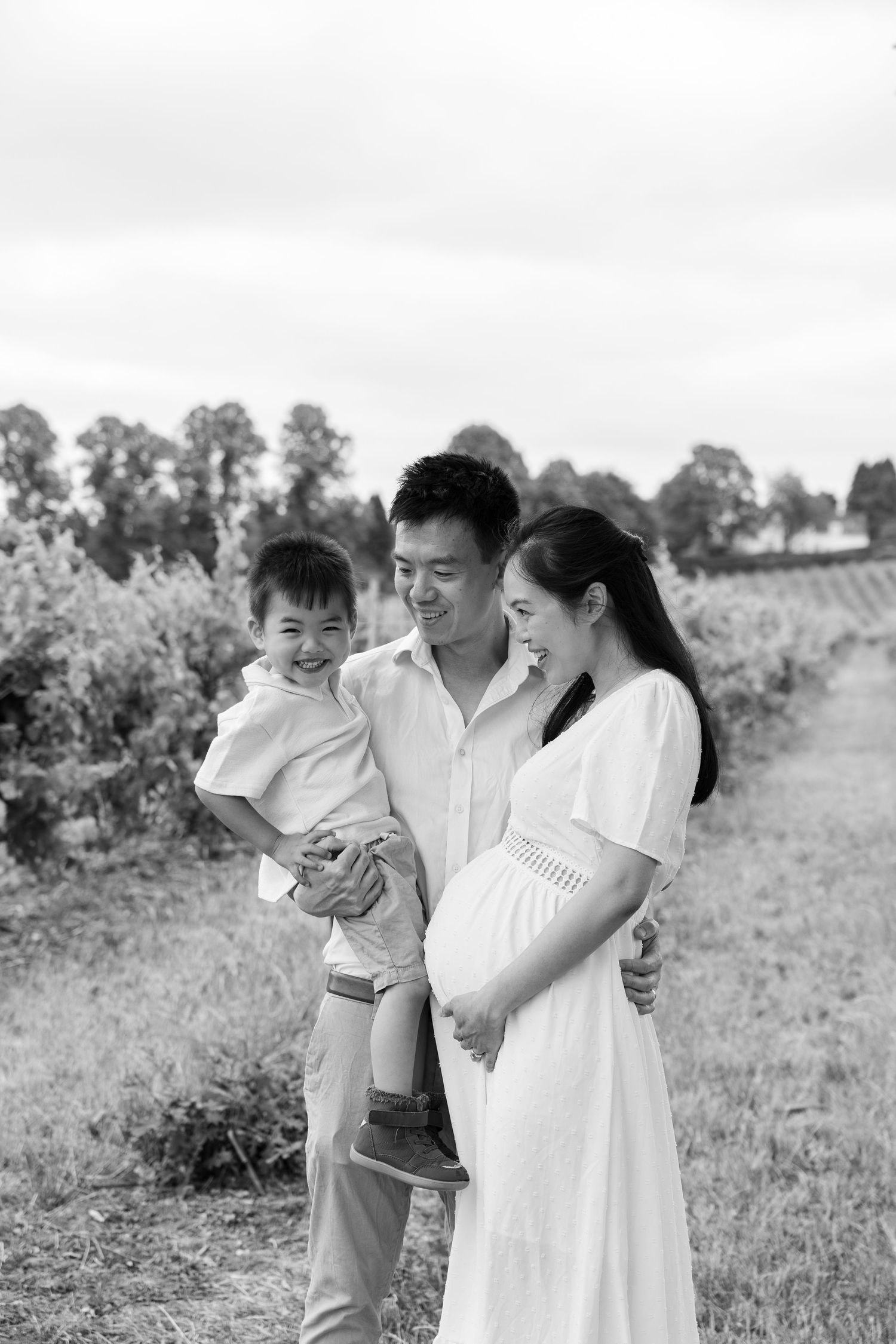 A family in white outfits stands together in a grassy field with trees in the background.