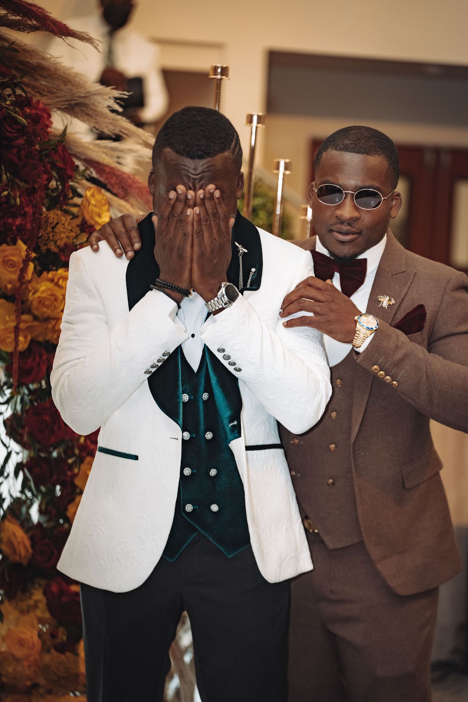 Two men at a formal event wearing stylish tuxedos, one in white and green and one in brown, posing at a celebration.