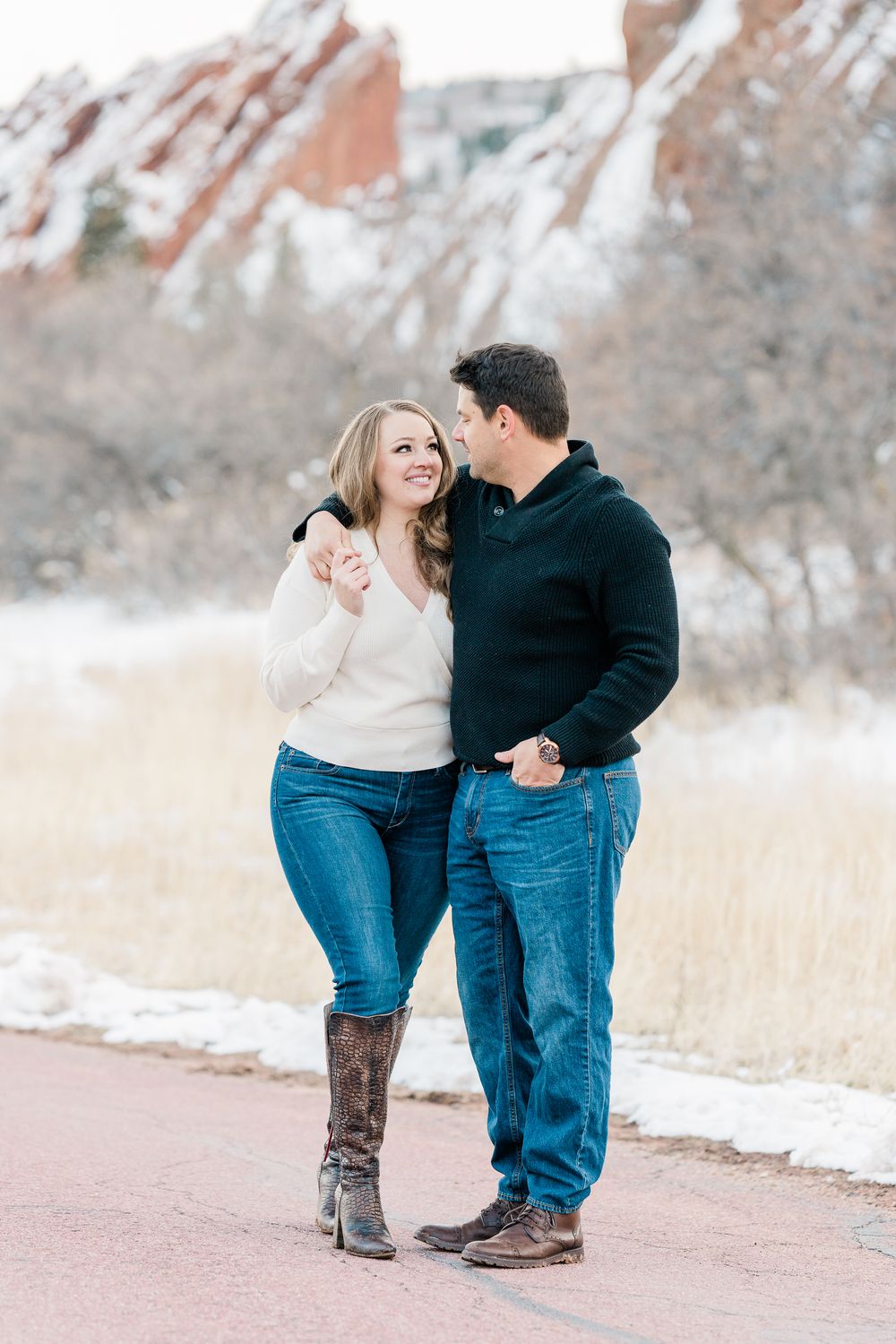A couple embraces while standing on a path with red rocks and snowy landscape in the background at Garden of the Gods.
