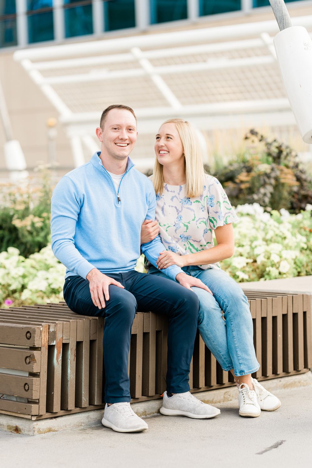 A couple sits casually together on a wooden bench, sharing laughter and conversation in an outdoor setting.