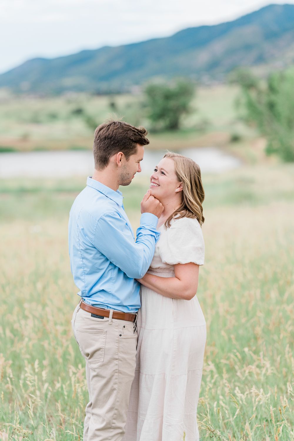 A romantic photoshoot showing tender moments between a couple in a sunny mountain meadow field.