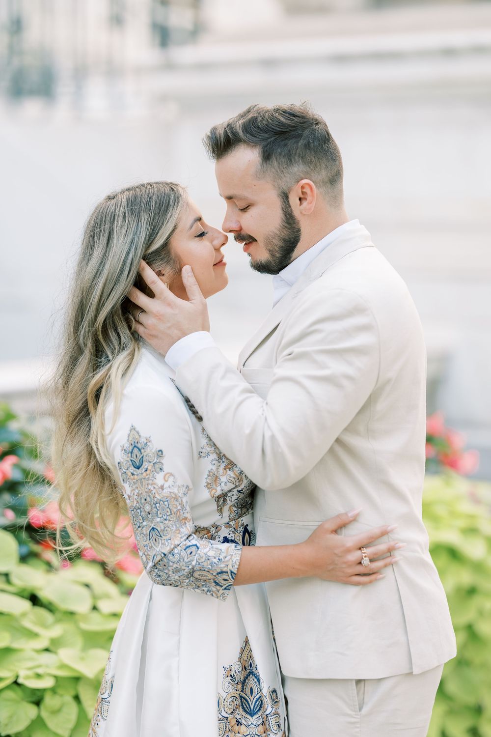 Romantic couple in white formal attire embrace tenderly in a garden setting with soft lighting.