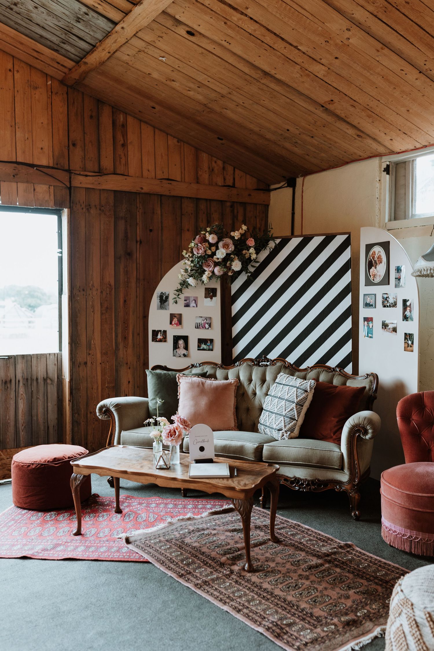 Cozy rustic wedding sitting area with wooden walls, vintage furniture, striped accent wall and plush pink velvet seating.