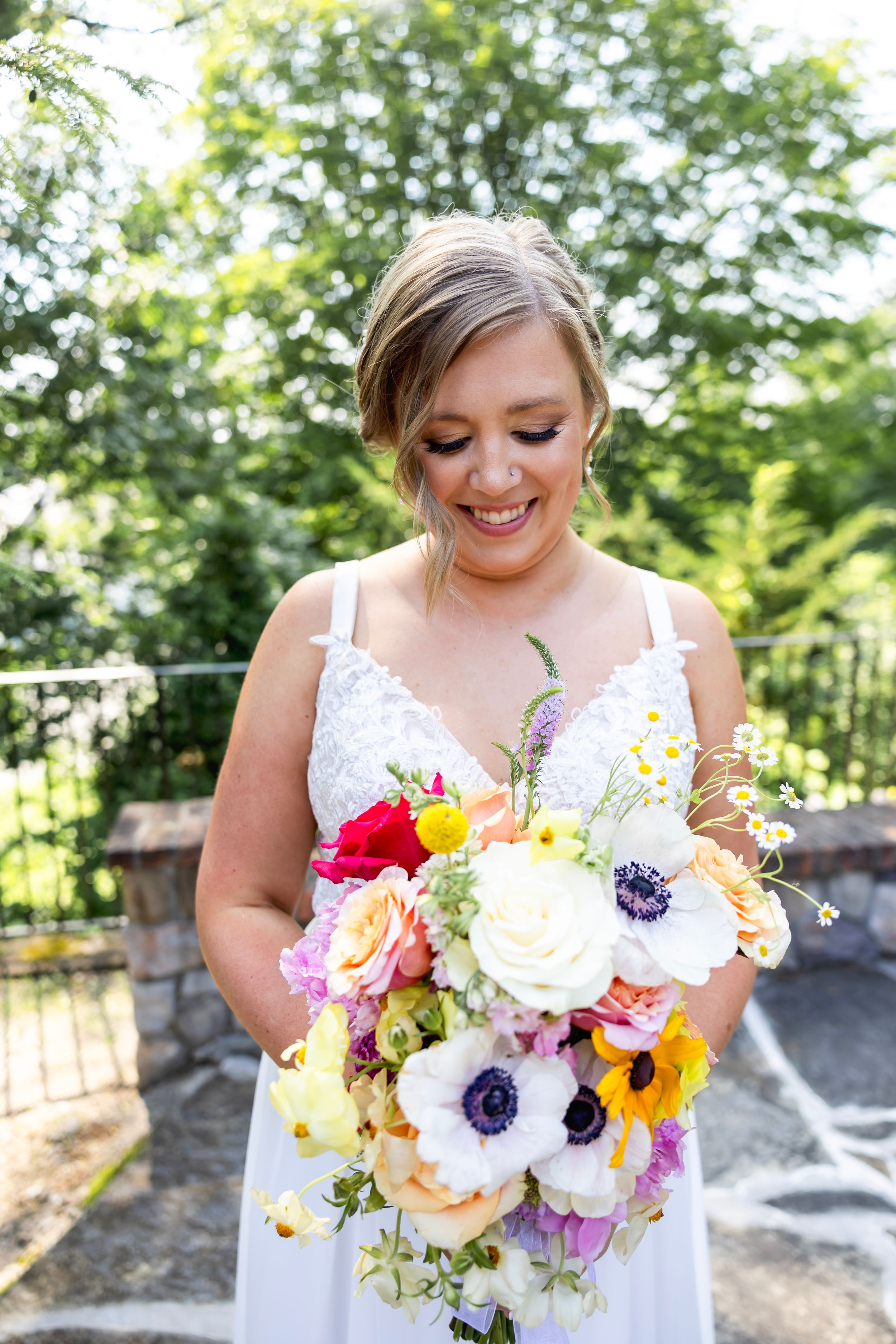 Bride in wedding dress holding vibrant bouquet with pink, yellow, and purple flowers against outdoor backdrop. NJ wedding photographer