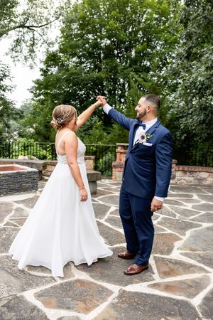 Couple in wedding attire dancing together on a stone patio surrounded by lush green trees. NJ wedding photographer | best NJ wedding photogr